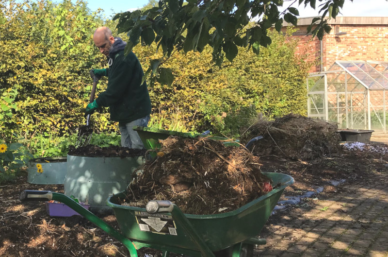 Emptying compost from a green johanna compost bin into a wheelbarrow to use. 