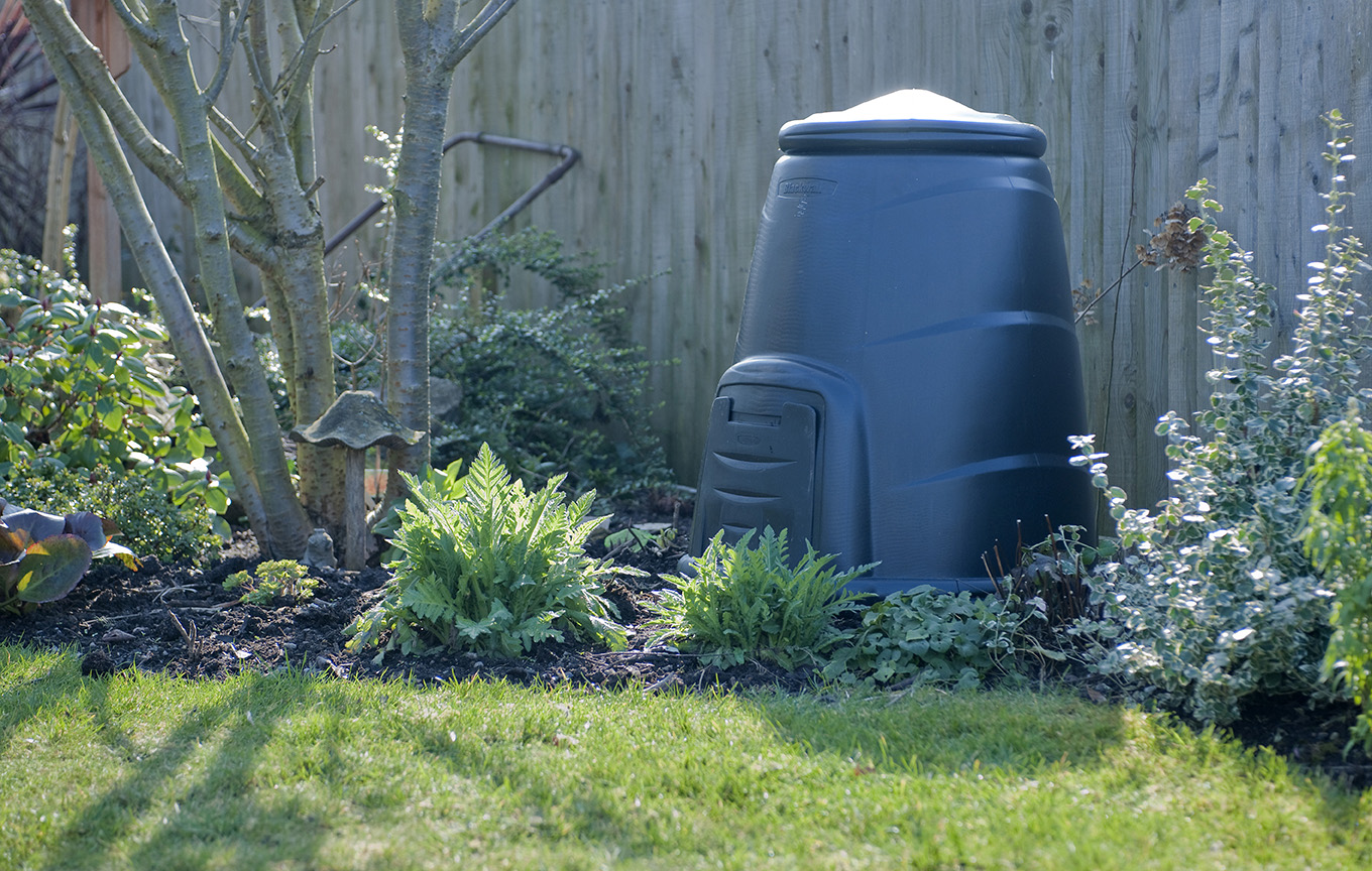 A black plastic compost bin within a home garden setting.